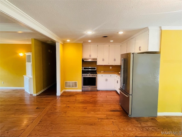 kitchen featuring appliances with stainless steel finishes, light wood-type flooring, a textured ceiling, white cabinetry, and ornamental molding