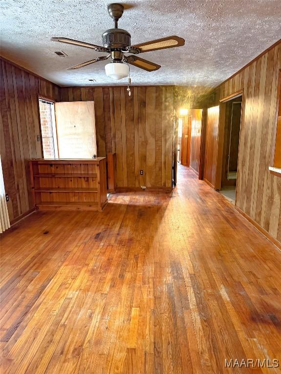 empty room with hardwood / wood-style floors, a textured ceiling, radiator, wood walls, and ceiling fan