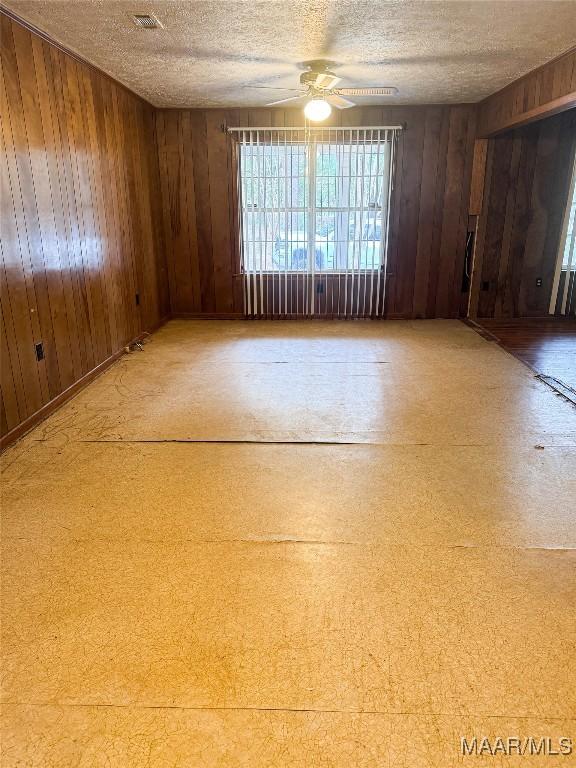 spare room featuring ceiling fan, wood walls, and a textured ceiling