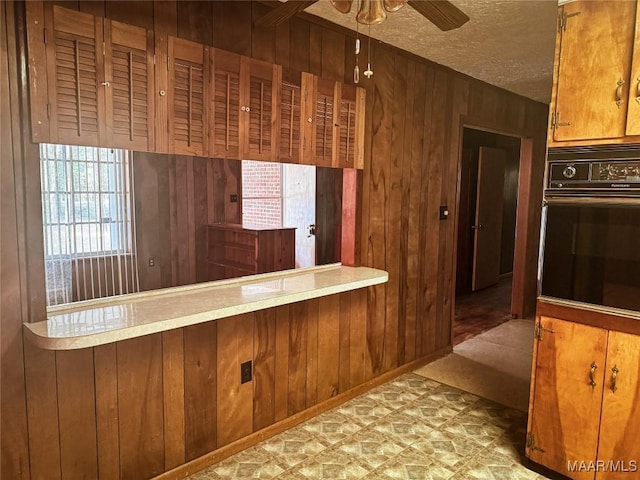 kitchen with a textured ceiling, ceiling fan, wood walls, and oven