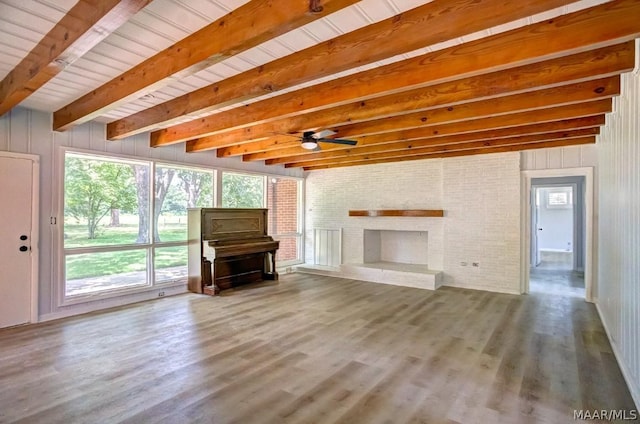 unfurnished living room featuring wood walls, wood-type flooring, ceiling fan, a brick fireplace, and beam ceiling