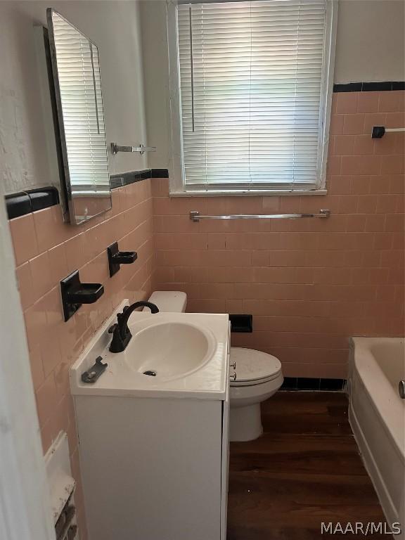 bathroom with toilet, wood finished floors, tile walls, vanity, and a bath