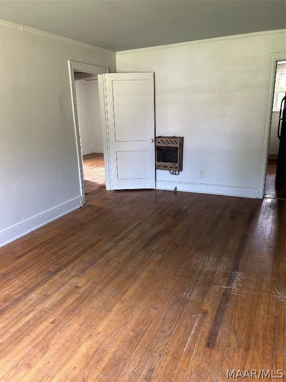 unfurnished bedroom featuring baseboards, crown molding, wood-type flooring, and heating unit