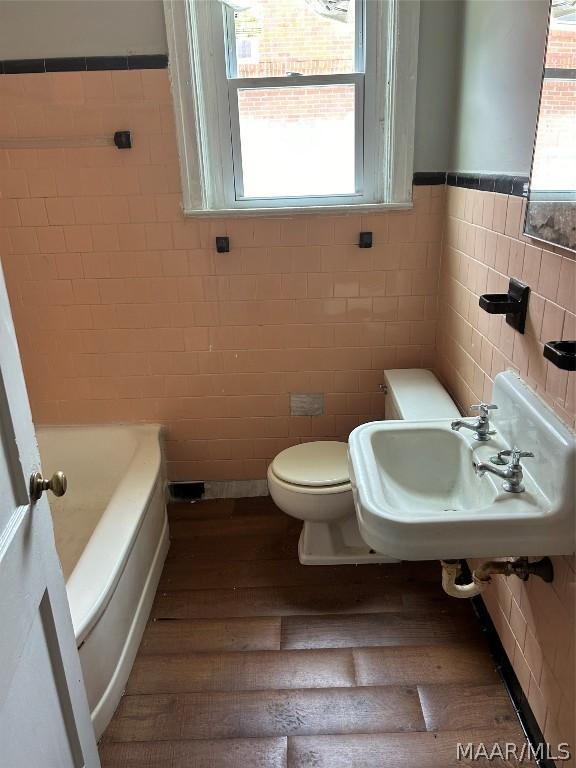 full bathroom featuring a tub, a wealth of natural light, toilet, and wood finished floors