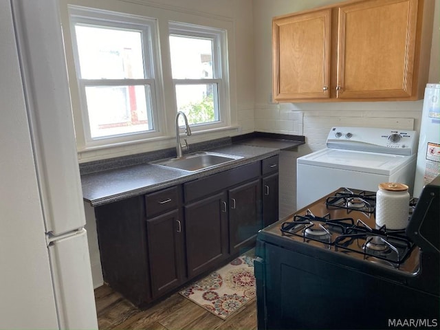 kitchen featuring washer / dryer, wood-type flooring, white refrigerator, black gas range oven, and sink