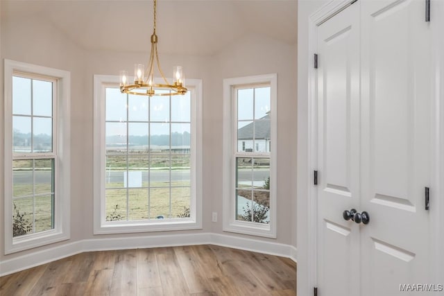 unfurnished dining area featuring lofted ceiling, a chandelier, wood finished floors, and baseboards