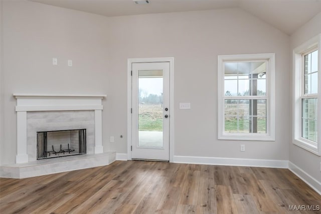 unfurnished living room with vaulted ceiling, a fireplace, wood finished floors, and a wealth of natural light