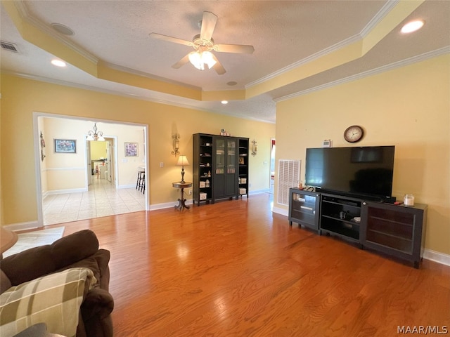 living room featuring ornamental molding, a raised ceiling, ceiling fan with notable chandelier, and light hardwood / wood-style flooring