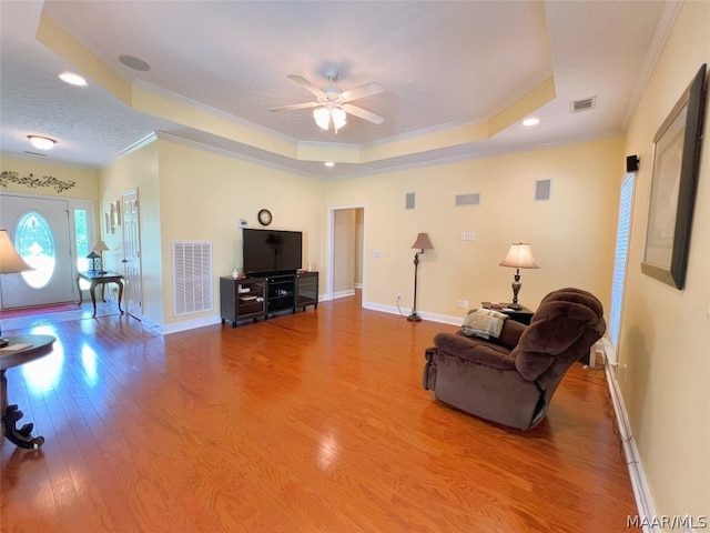 living room featuring a raised ceiling, crown molding, and hardwood / wood-style floors