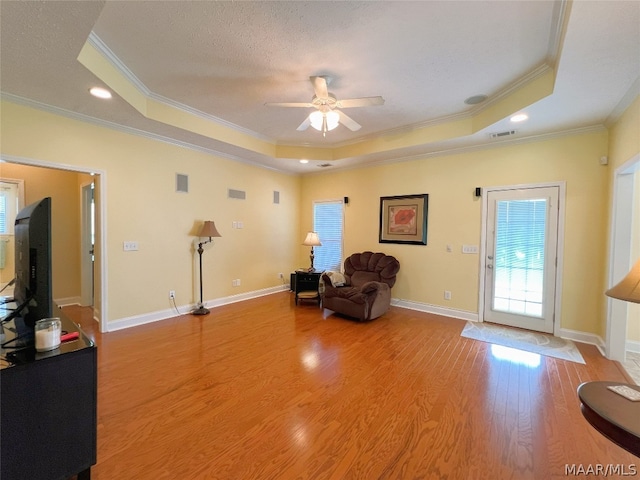 living area featuring ornamental molding, a raised ceiling, and light wood-type flooring