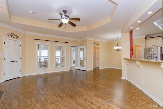 unfurnished living room featuring ceiling fan with notable chandelier, wood-type flooring, and a raised ceiling