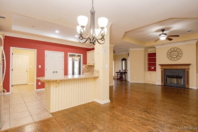 kitchen with pendant lighting, kitchen peninsula, a kitchen breakfast bar, light hardwood / wood-style floors, and a tray ceiling