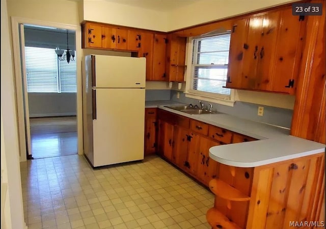 kitchen featuring light tile patterned flooring, white fridge, kitchen peninsula, hanging light fixtures, and sink