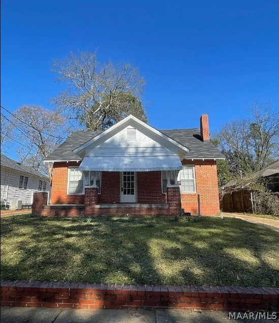 view of front facade with brick siding, a front lawn, a chimney, and covered porch