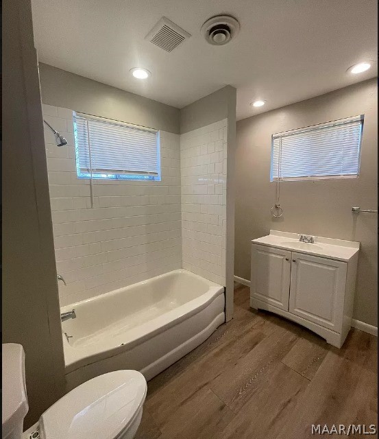 full bathroom with tiled shower / bath combo, toilet, wood-type flooring, and a healthy amount of sunlight