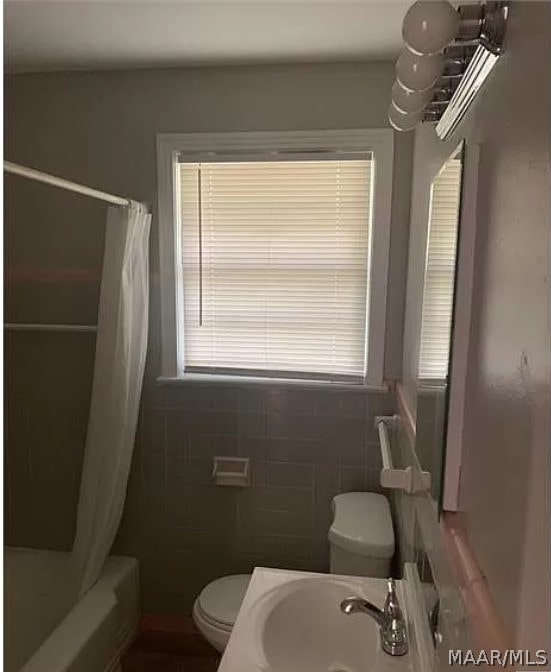 full bathroom with tile walls, shower / bath combo with shower curtain, toilet, and sink