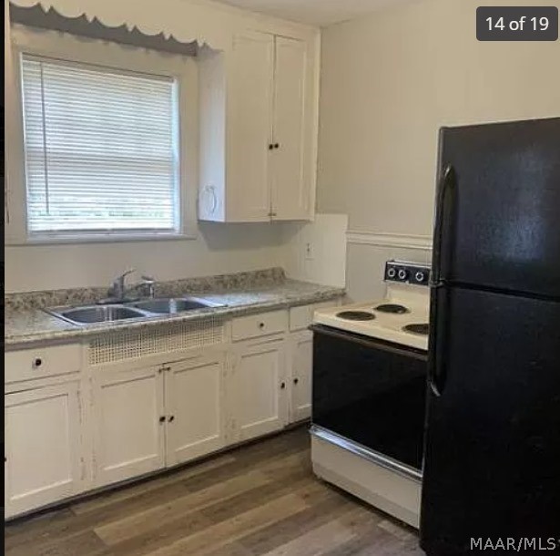 kitchen featuring sink, white electric range oven, black refrigerator, white cabinetry, and hardwood / wood-style flooring