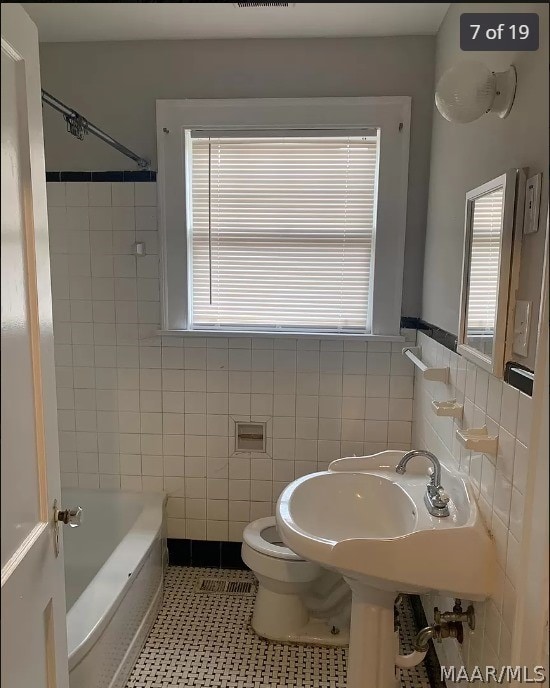 bathroom featuring tile patterned flooring, tile walls, toilet, and a wealth of natural light