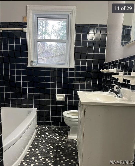 bathroom featuring toilet, vanity, tile patterned flooring, and tile walls