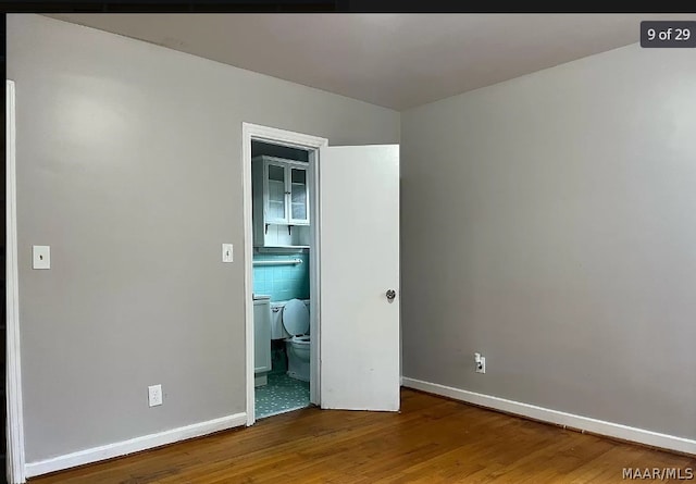 unfurnished bedroom with ensuite bathroom, tile walls, and wood-type flooring