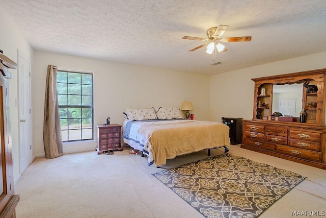 bedroom featuring a textured ceiling, light colored carpet, and ceiling fan