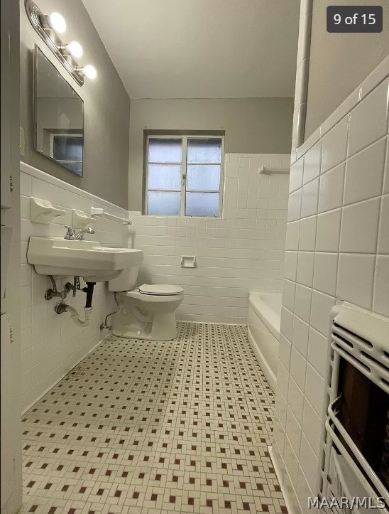 bathroom featuring radiator heating unit, washtub / shower combination, toilet, tile walls, and tile patterned floors