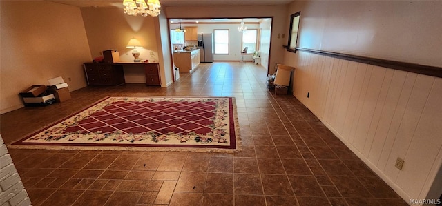 corridor with a chandelier, dark tile patterned flooring, a wainscoted wall, and wood walls