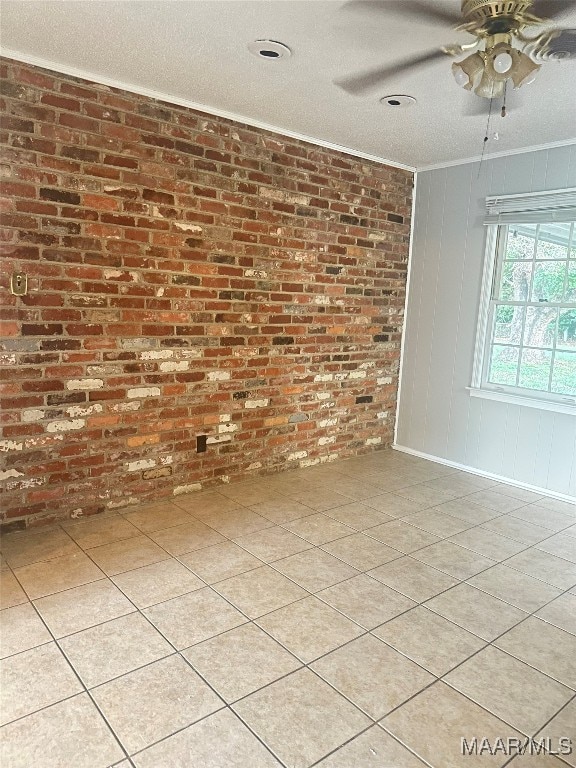 unfurnished room featuring a textured ceiling, light tile patterned floors, ornamental molding, ceiling fan, and brick wall