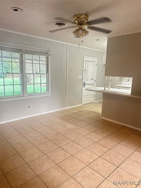 tiled empty room featuring ceiling fan, a textured ceiling, wooden walls, and ornamental molding