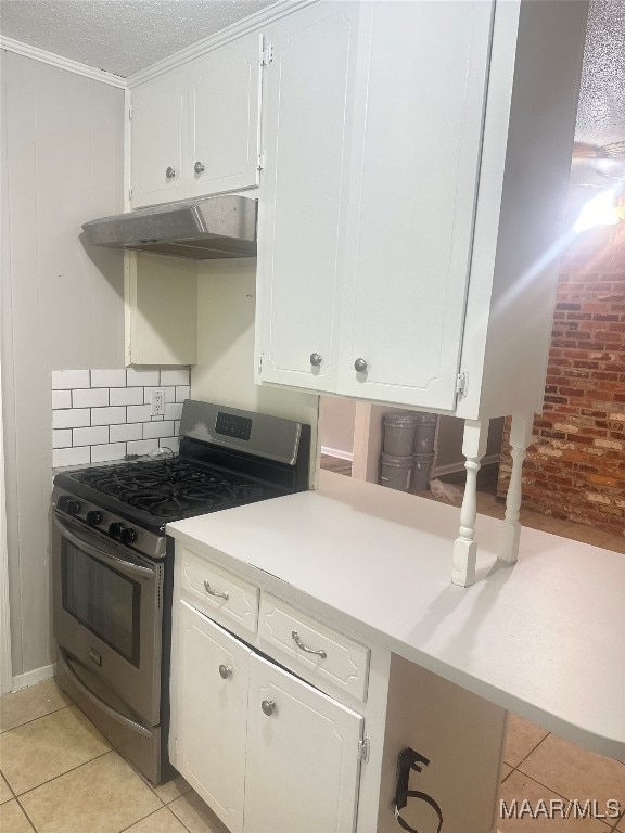 kitchen with stainless steel gas range oven, light tile patterned floors, exhaust hood, and white cabinets