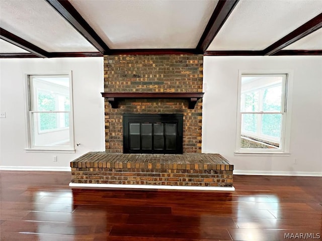 unfurnished living room featuring beam ceiling, a brick fireplace, a healthy amount of sunlight, and dark hardwood / wood-style flooring