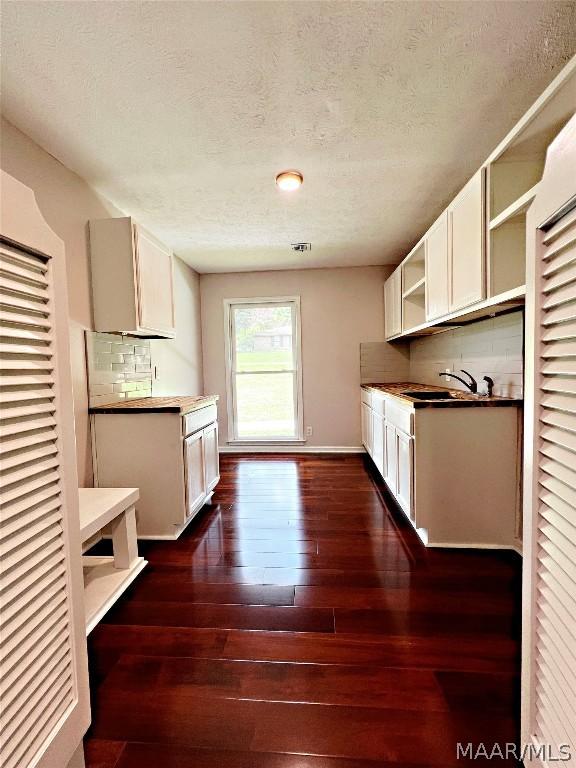 kitchen with sink, tasteful backsplash, white cabinetry, a textured ceiling, and dark hardwood / wood-style flooring