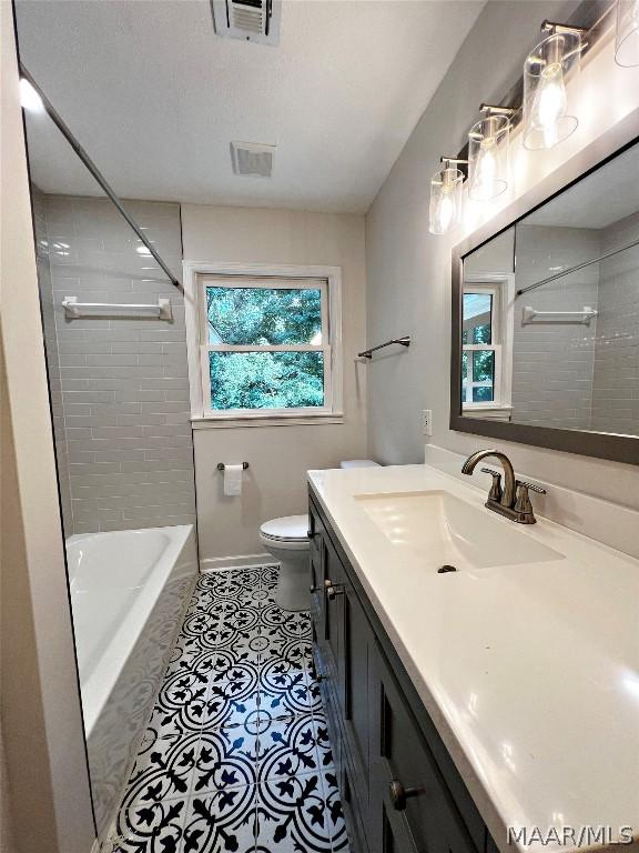 full bathroom featuring tile patterned flooring, vanity, tiled shower / bath combo, and toilet