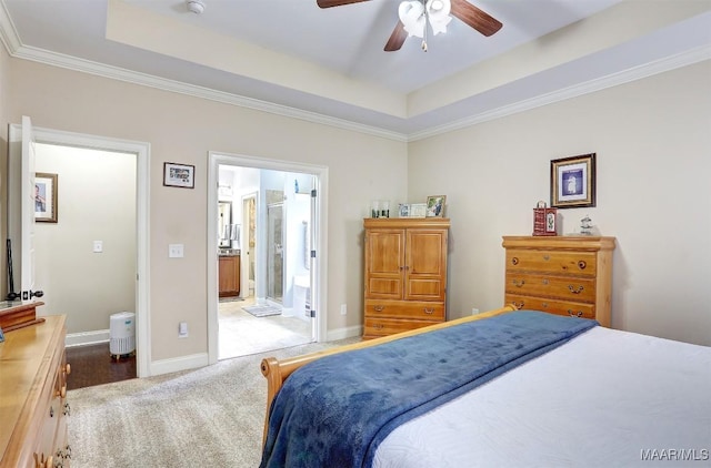 bedroom with ceiling fan, ensuite bathroom, a tray ceiling, and light carpet