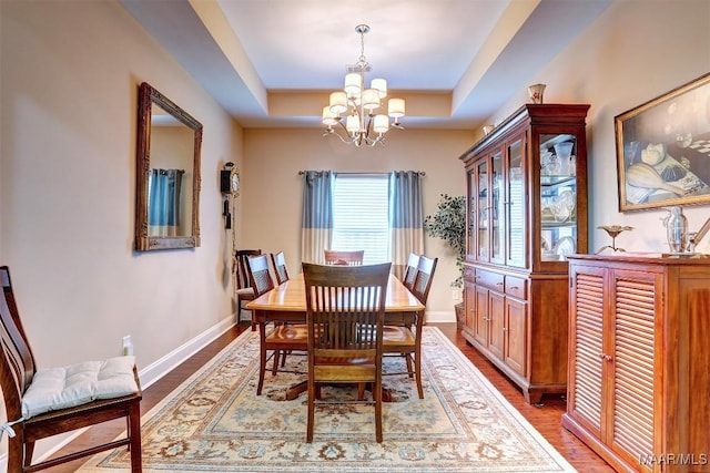 dining area with hardwood / wood-style floors, a notable chandelier, and a raised ceiling