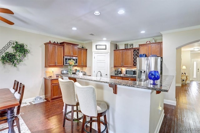 kitchen featuring dark hardwood / wood-style flooring, a kitchen breakfast bar, dark stone counters, a kitchen island with sink, and stainless steel appliances