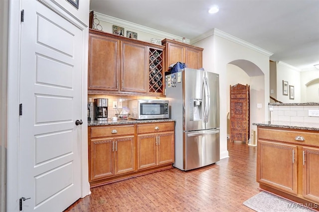 kitchen featuring stainless steel appliances, crown molding, decorative backsplash, and dark stone counters