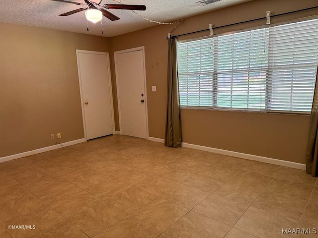 empty room with ceiling fan, light tile patterned floors, and a textured ceiling