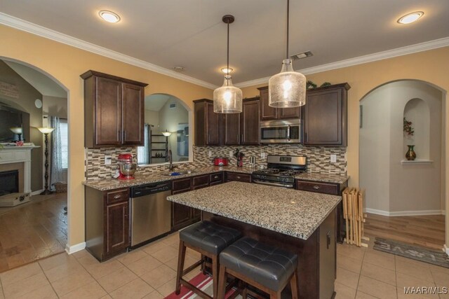 kitchen featuring light tile patterned flooring, a kitchen bar, a center island, stainless steel appliances, and light stone countertops