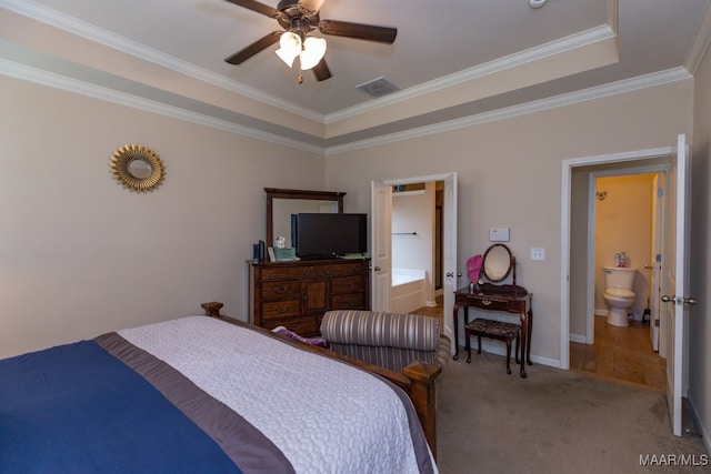 carpeted bedroom with a tray ceiling, ornamental molding, ceiling fan, and ensuite bathroom