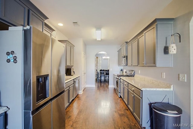 kitchen featuring gray cabinets, appliances with stainless steel finishes, dark hardwood / wood-style floors, light stone countertops, and an inviting chandelier