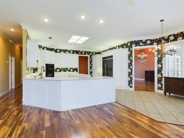 kitchen with built in fridge, kitchen peninsula, light tile patterned floors, a chandelier, and white cabinetry