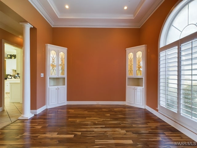 spare room featuring built in features, decorative columns, crown molding, and hardwood / wood-style floors