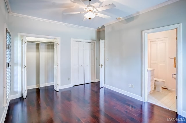 unfurnished bedroom with ceiling fan, two closets, dark hardwood / wood-style flooring, ornamental molding, and ensuite bathroom