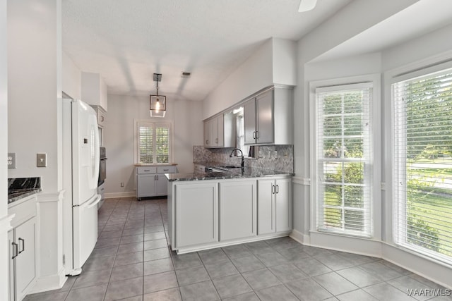 kitchen featuring tasteful backsplash, white refrigerator, kitchen peninsula, decorative light fixtures, and light tile patterned flooring