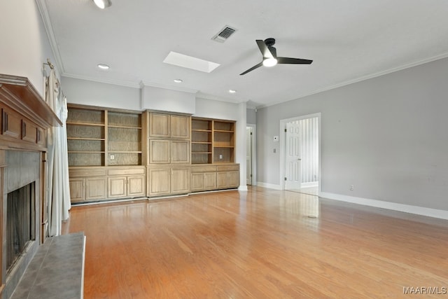 unfurnished living room with a fireplace, ceiling fan, light wood-type flooring, a skylight, and ornamental molding