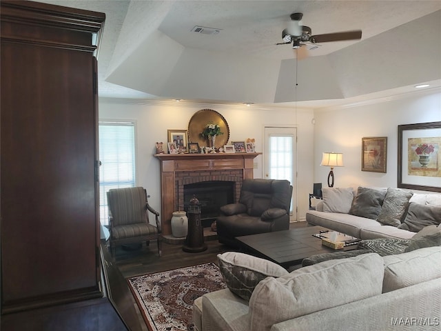 living room featuring ceiling fan, a tray ceiling, hardwood / wood-style flooring, and a brick fireplace