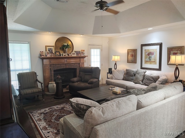 living room with ceiling fan, a brick fireplace, hardwood / wood-style flooring, a raised ceiling, and ornamental molding