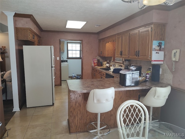 kitchen with kitchen peninsula, light tile patterned floors, washer / dryer, decorative backsplash, and white fridge