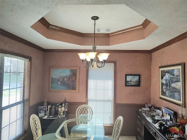 dining area with an inviting chandelier, a textured ceiling, crown molding, and a raised ceiling